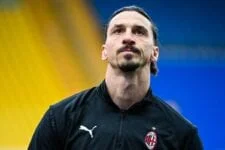 En fotballspiller som ligner Zlatan Ibrahimovic i en svart Milan-jakke med en Puma-logo, og ser i det fjerne med fokus.