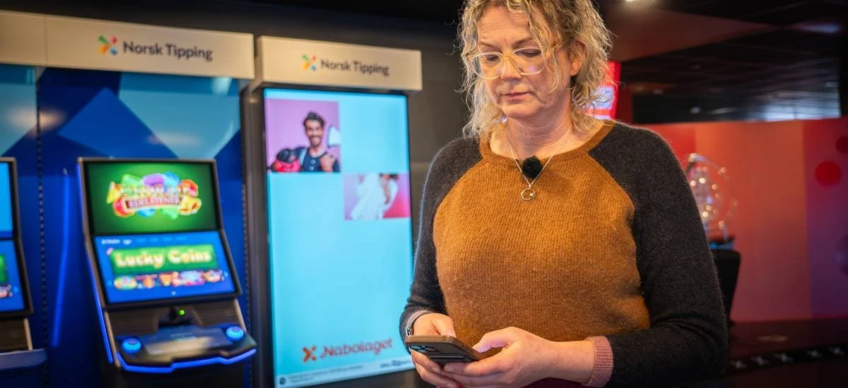 Kvinne som bruker mobiltelefon foran Norsk Tipping-automater